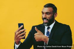 Smiling Black businessman in suit giving thumbs up at smartphone screen bDBG85