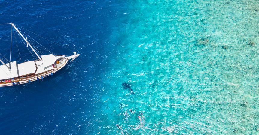 Aerial shot of boat with people swimming in tropical waters, wide