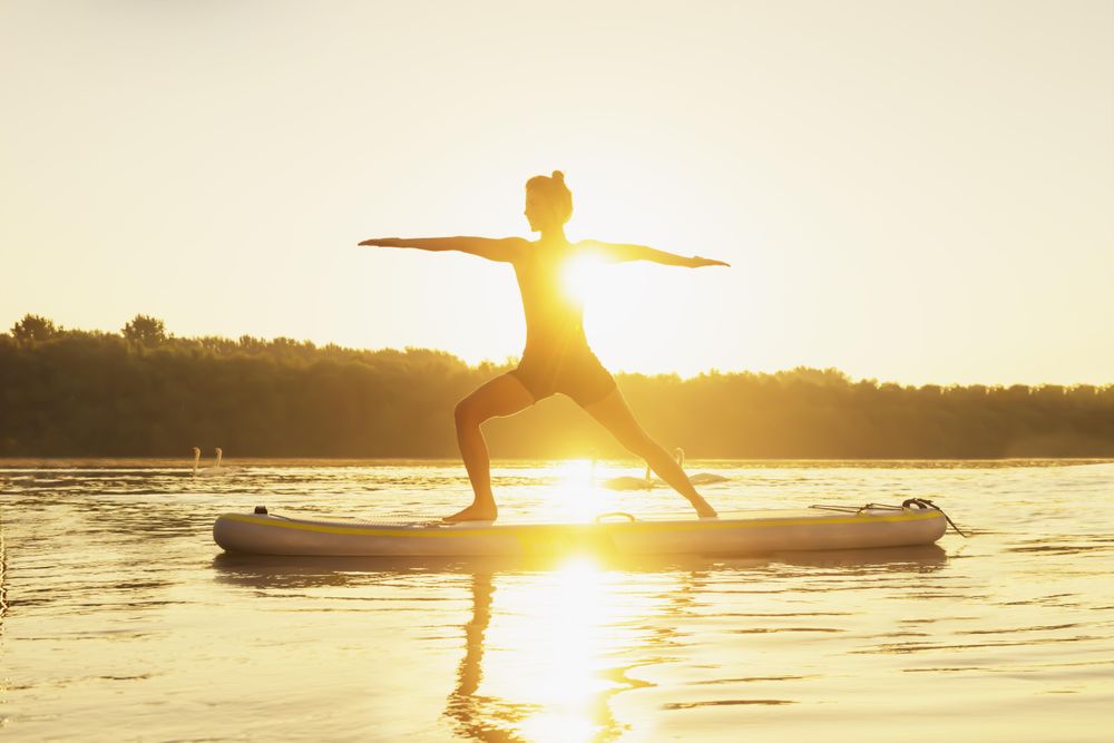 Silhouette of woman standing in warrior pose during sunset