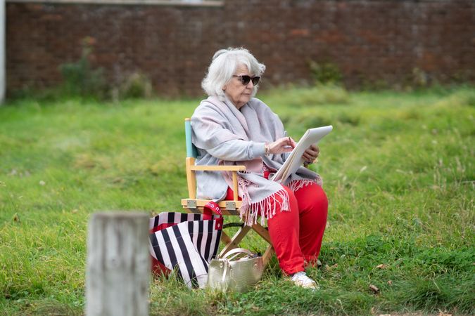 Older woman sitting outside in park at drawing class in sunglasses