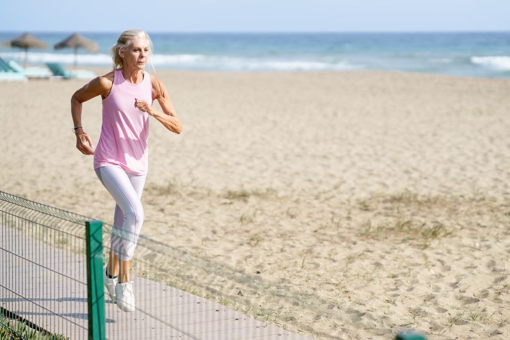Older woman in sports gear running along beach