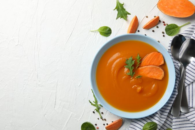 Sweet potato soup on table with salt pepper and spoons with copy space