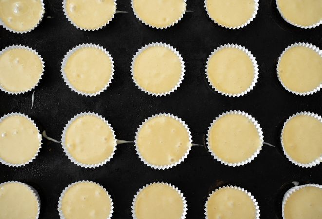Some paper molds on a baking tray are filled with cupcakes dough