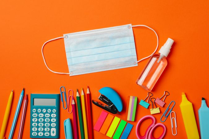 School supplies with medical mask and sanitizer on orange background