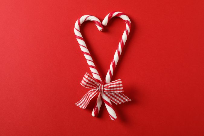 Sweet candy canes with bow on red background, space for text