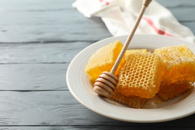 Plate with dipper and honeycombs on wooden background, space for text