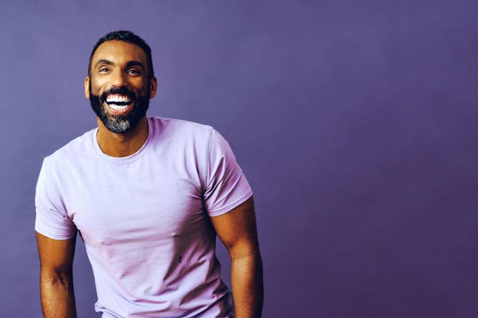 Smiling male in purple studio with hands in pocket, copy space