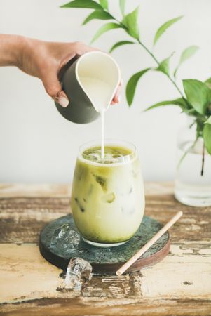 Iced matcha drink with hand pouring cream from pitcher