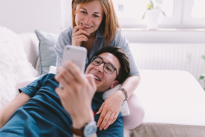 Couple happily lounging looking at a smartphone together