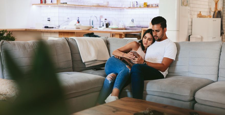 Young couple relaxing on couch with smart phone at home in the living room