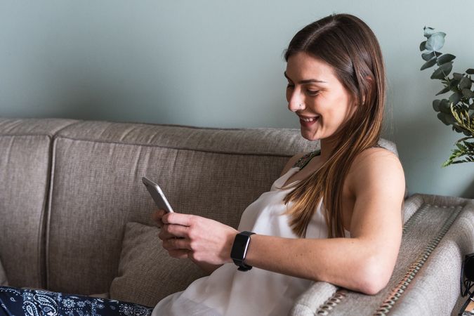Woman chatting on smartphone on sofa at home