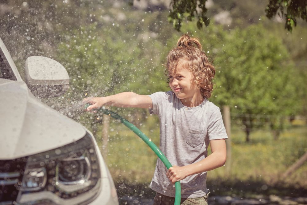 Cheerful boy splashing water on car