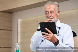Grey haired doctor checking notes phone 5RRaN5