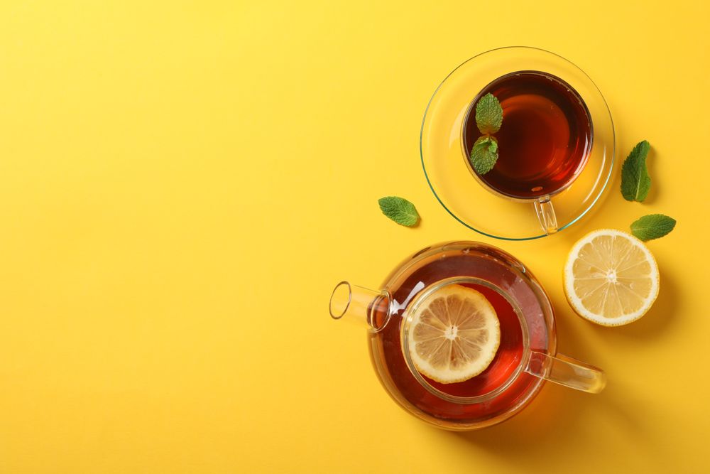 Flat lay. Cup of tea, teapot, lemon and mint on yellow background, copy space