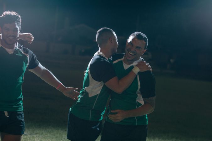 Sportsmen in uniform hugging and smiling after winning a rugby game
