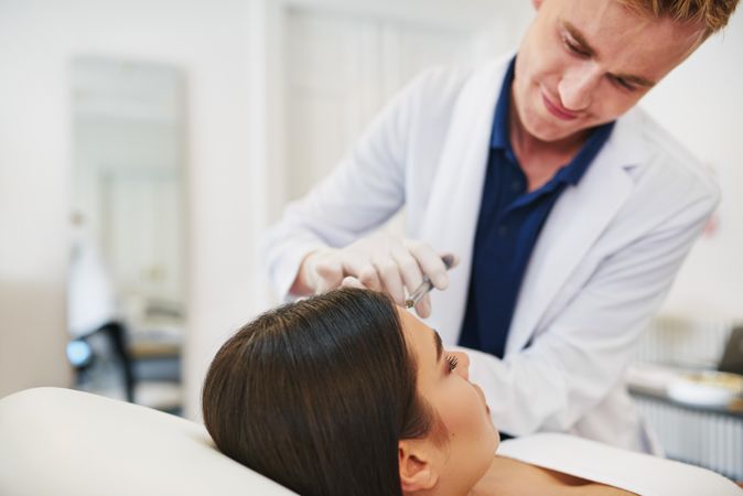 Smiling male dermatologist injecting treatment into patient’s face