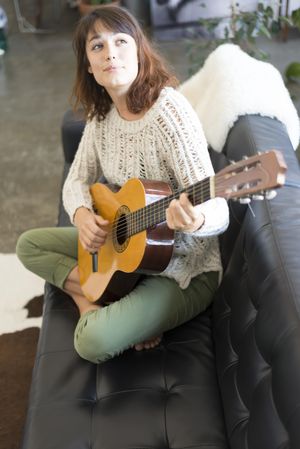 Female strumming guitar in living room of bright loft