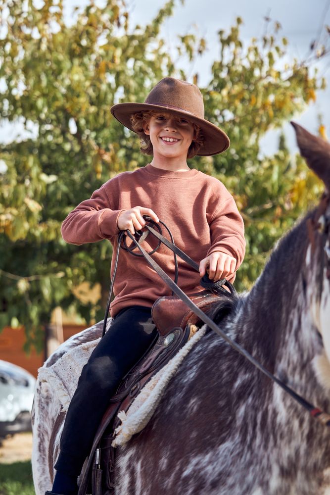 Boy in hat riding his brown mottled horse