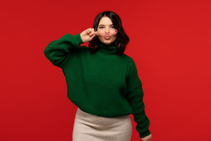 Woman in green sweater holding candy cane like mustache