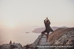 Woman in yoga pose next to castle wall overlooking sea 5wjGv0