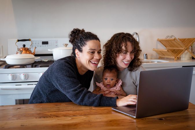 Cute young family smiling and looking at a laptop at kitchen table with baby