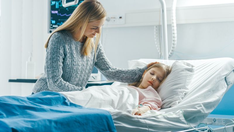 Cute Little Girl Sleeps on a Bed in the Children's Hospital, Caring Mother Covers Her with a Blanket and Caresses Her Forehead