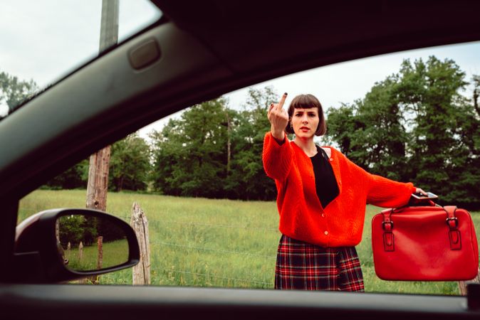 Woman in red sweater gesturing near car on road