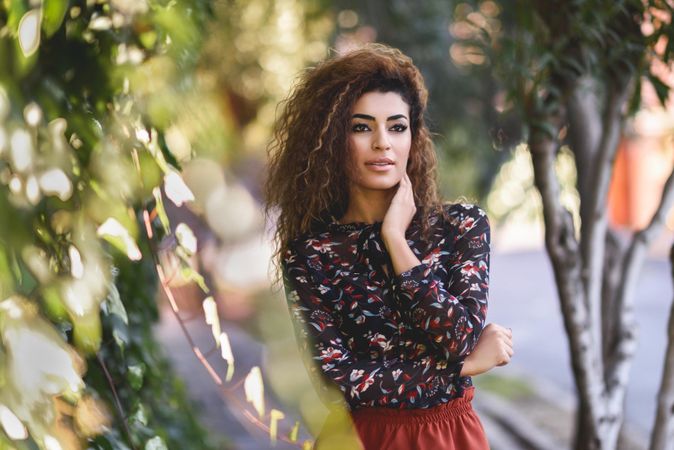 Wistful Arab woman wearing casual clothes in the street lined with greenery