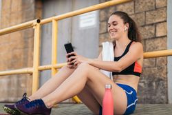 An athletic woman resting with her smartphone after running.
