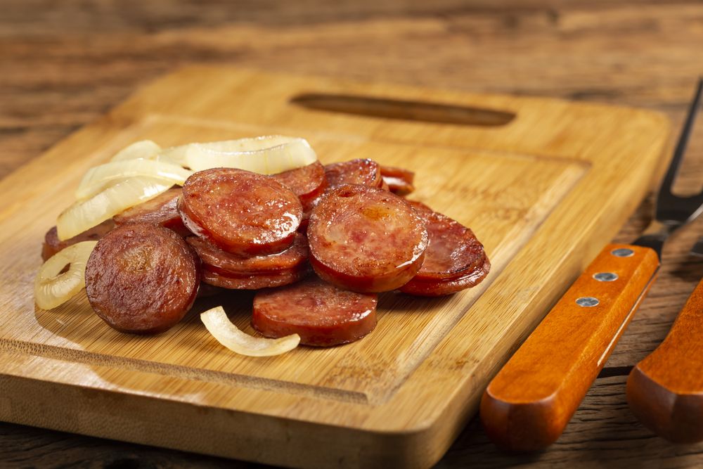 Sliced calabrese sausage with onion on wooden background.