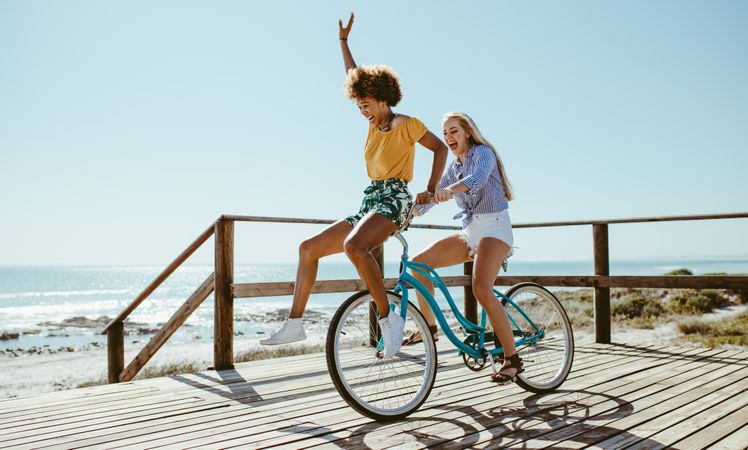 Cheerful young women taking a bike ride together at the beach