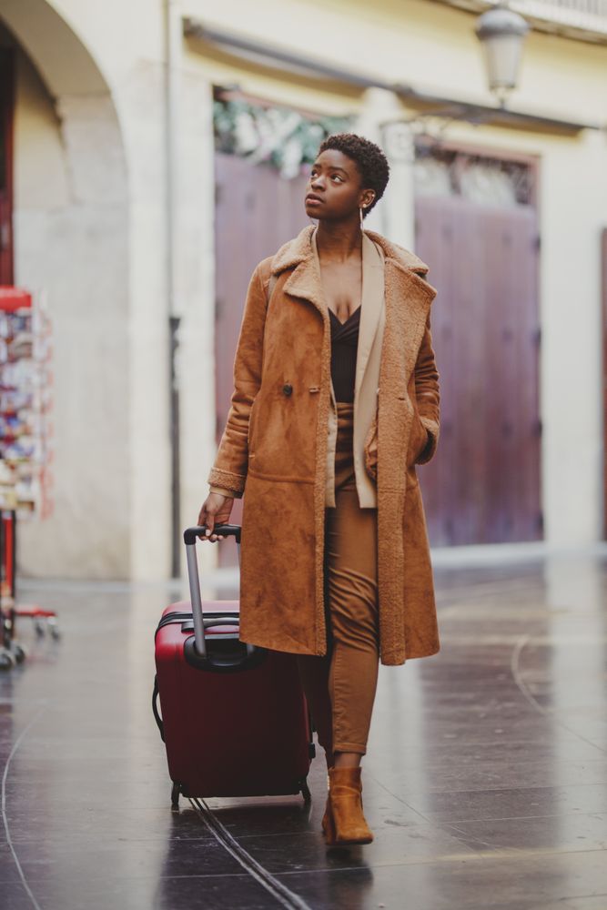 Stylish Black woman with luggage walking on street