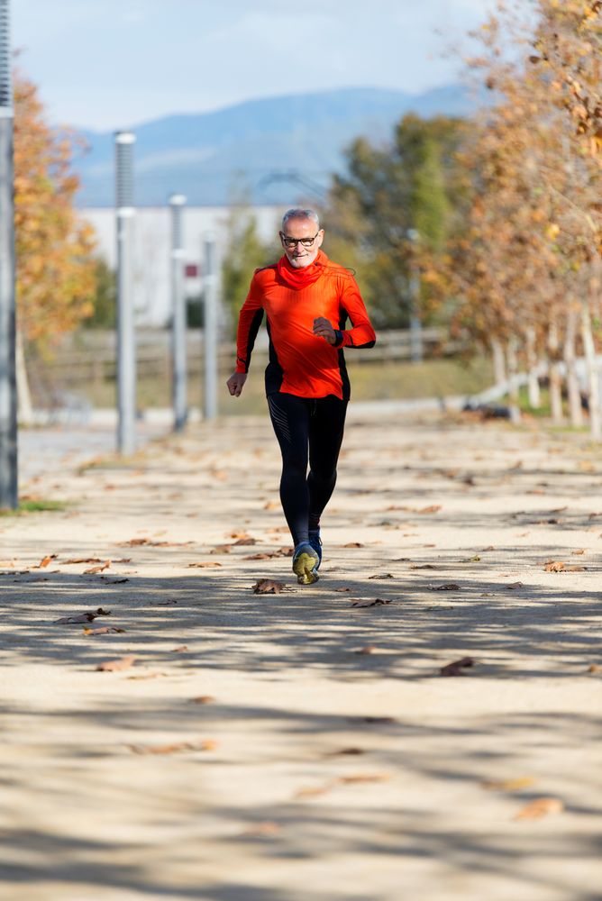 Male in red wind breaker running through park