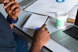 Black male writing in notepad near laptop in office