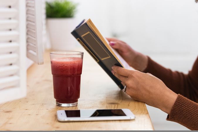 Anonymous Black woman drinking smoothie and reading book in bar