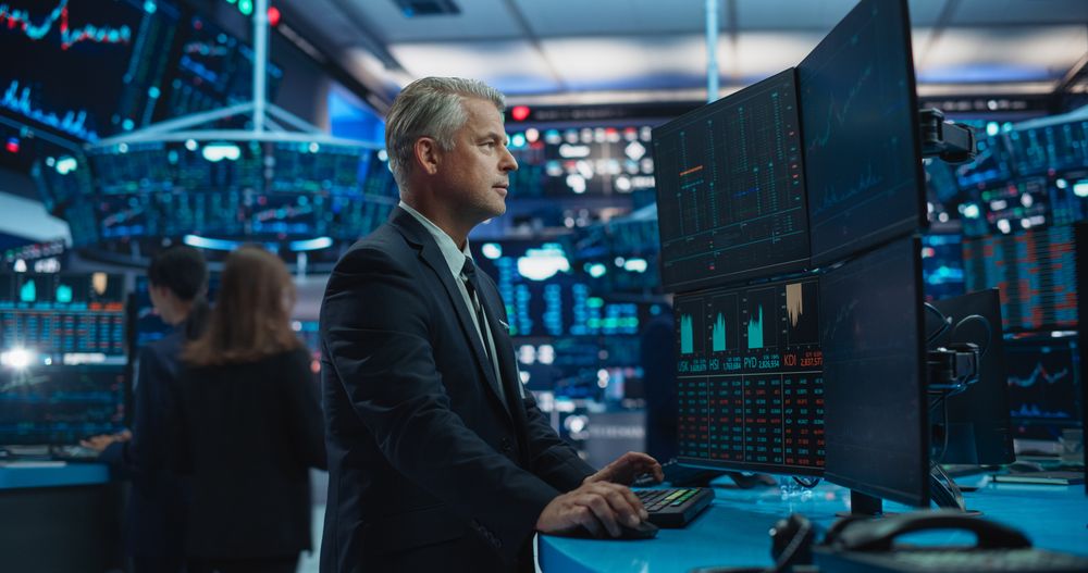 Financial Analyst Using Desktop Computer with Multi-Monitor Workstation with Real-Time Graphs, Financial Reports and Market Charts.