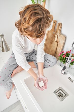 Kid washing hands with bar of soap in kitchen