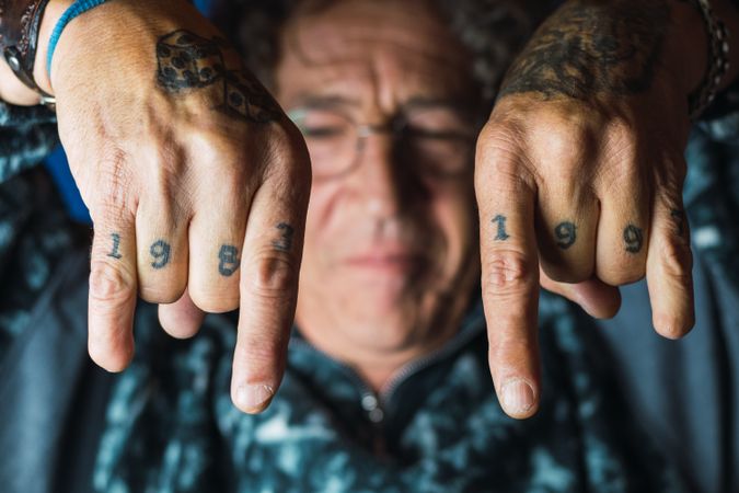 Positive tattooed mature man showing rock and roll gesture in studio