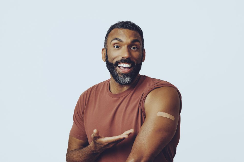 Smiing man pointing at arm arm with vaccination, copy space