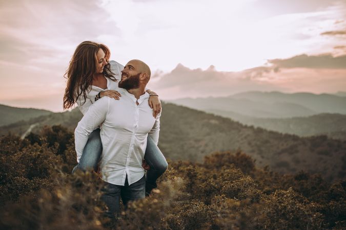 Affectionate couple riding piggyback along hilly valley