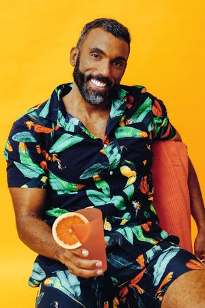 Happy Black male sitting down with cocktail in yellow room, vertical