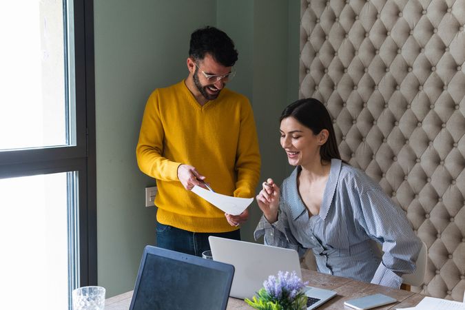 Cheerful colleagues discussing data on paper sheet in office