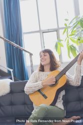 Happy female strumming guitar in living room of bright loft 41oaj0