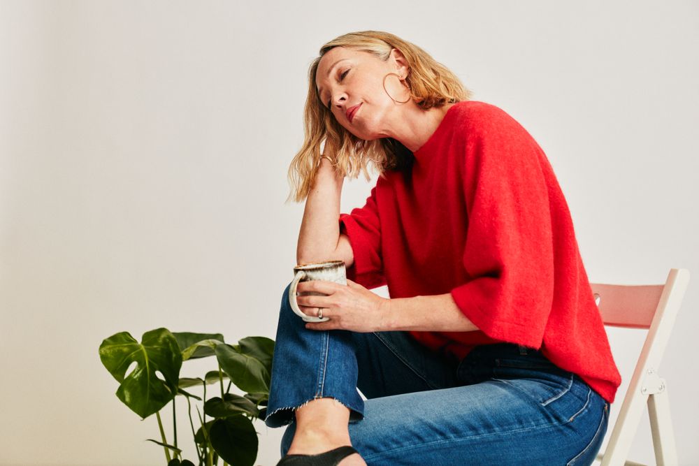 Woman in red jumper on chair leaning her head on her hand with eyes closed