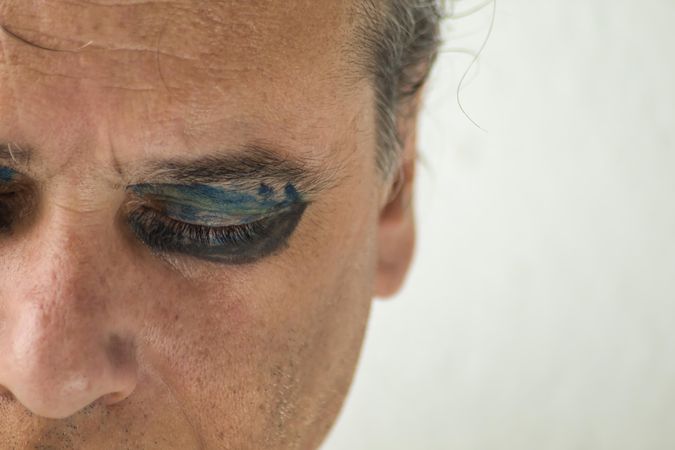 Middle aged man's closed right eye with dark and blue eyeshadow