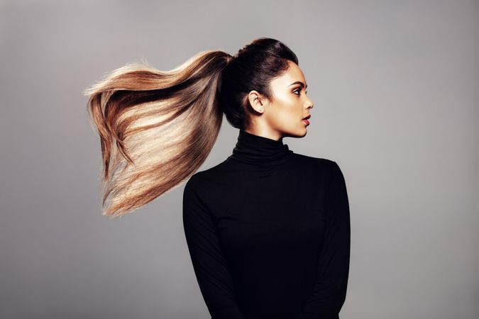Studio shot of stylish young woman with flying hair against grey background