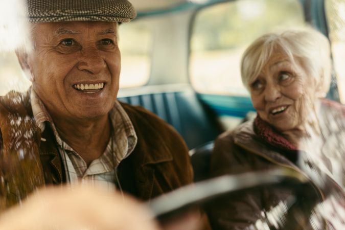 Smiling older man driving a car with woman on passenger seat