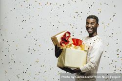 Smiling Black man holding pile of wrapped presents in both arms as glitter falls 5kP264