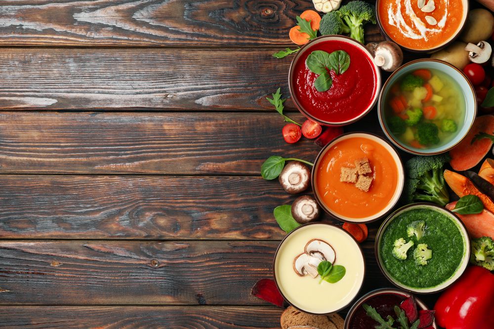 Top view of colorful soups on dark wooden table with copy space