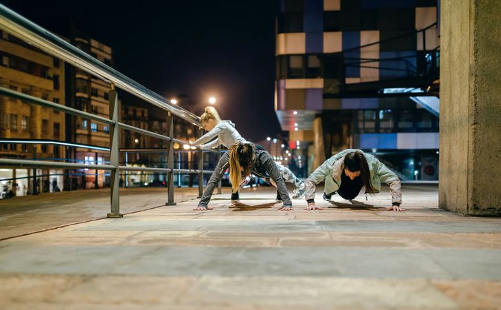 Female sport team doing push ups during training in the city at night